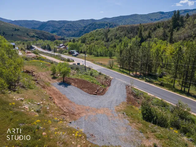 Gravel driveway with a paved road, surrounded by natural landscaping and mature trees