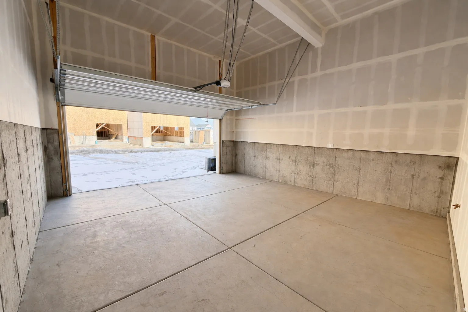 Concrete garage flooring with expansion joints, unfinished drywall, and exposed concrete foundation walls