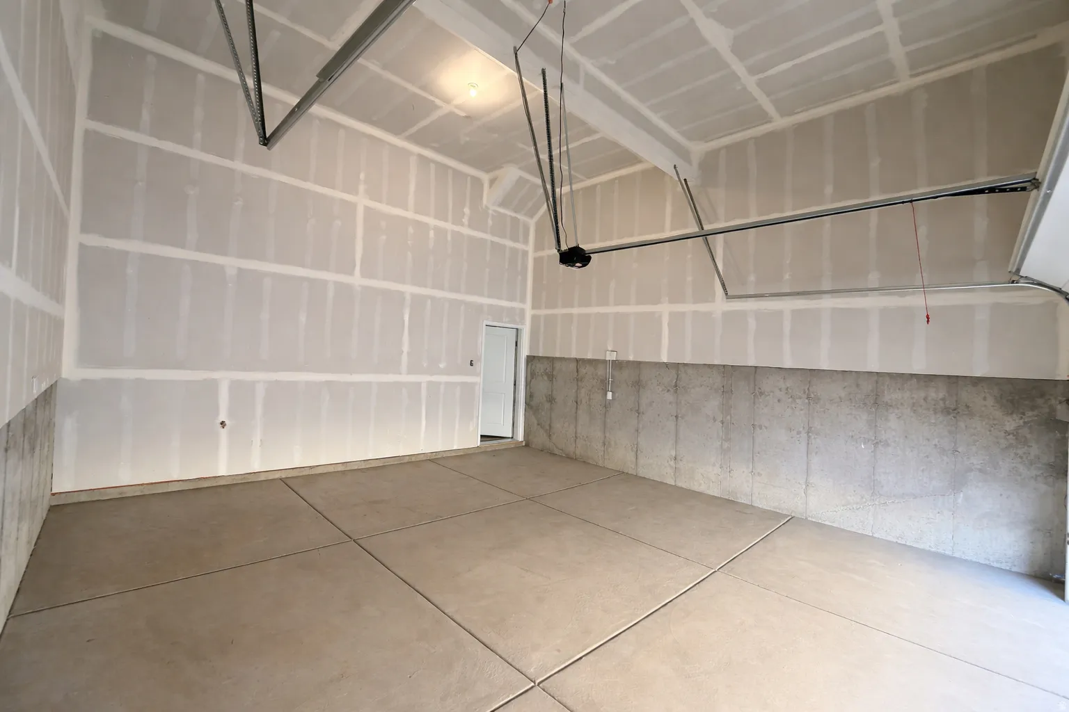 Expansive garage featuring a high vaulted ceiling, concrete flooring, and a standard side door