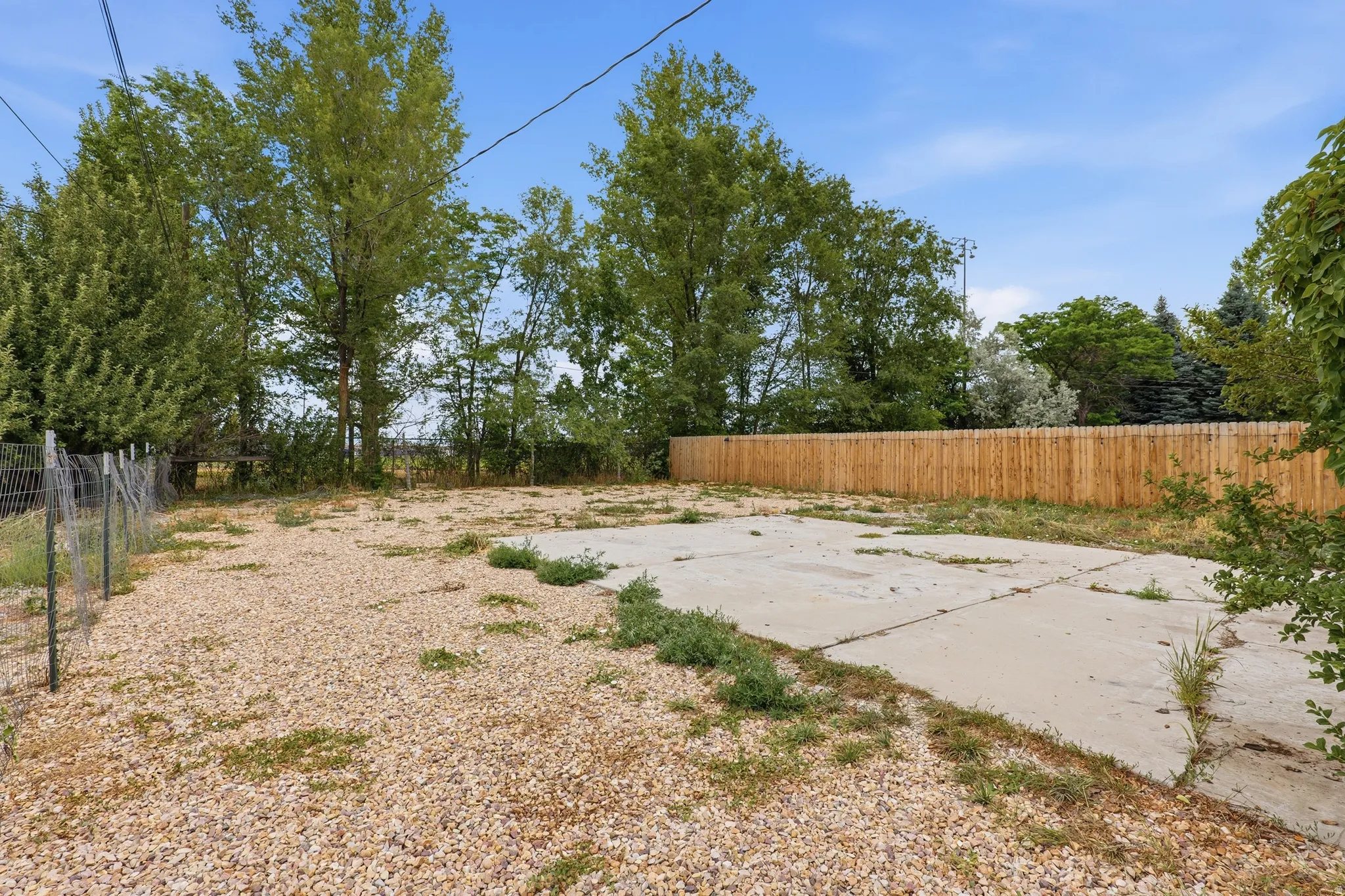 Expansive outdoor area featuring a concrete pad, gravel surfacing, a new wood privacy fence, and mature trees