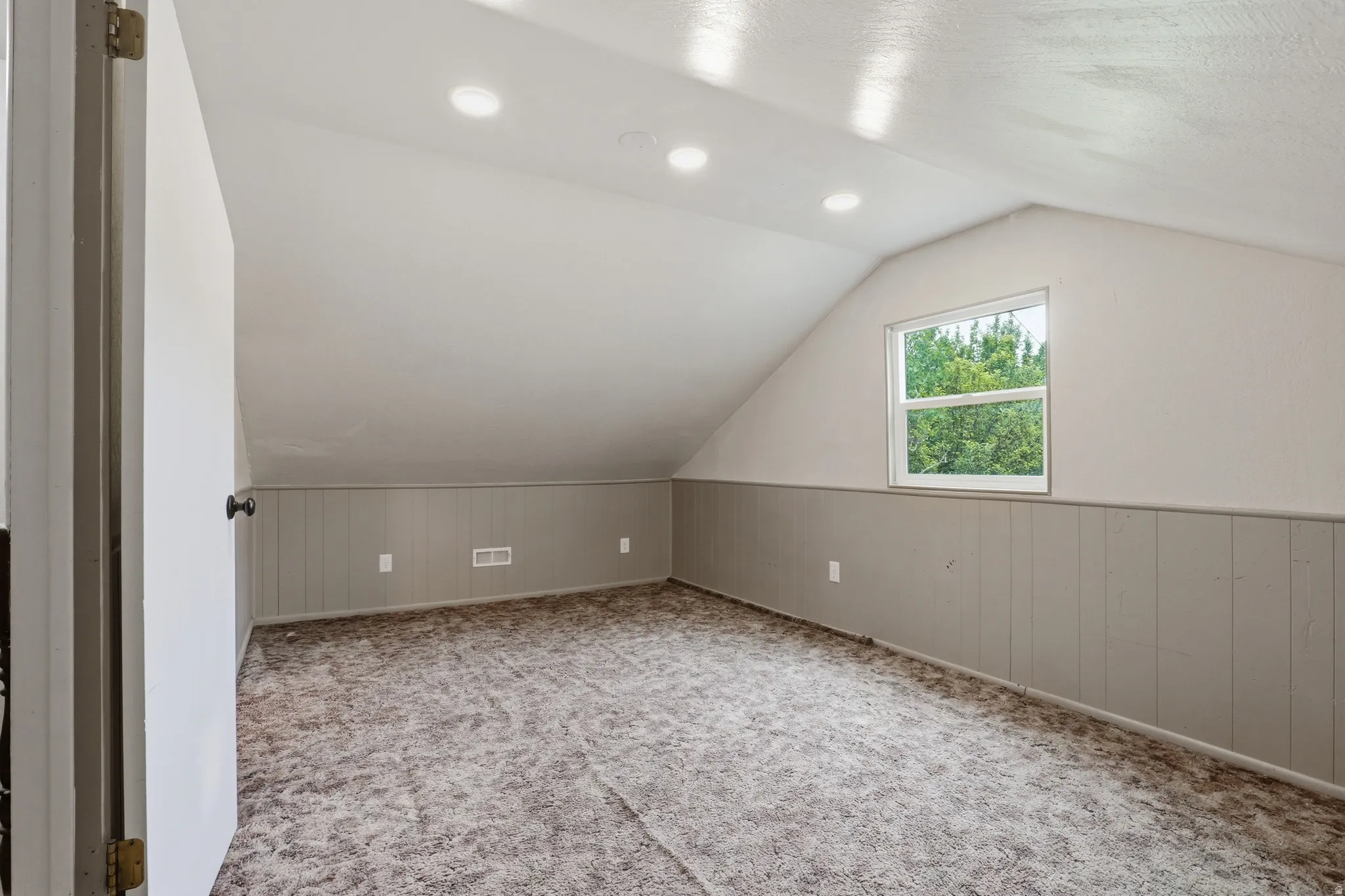 Attic room featuring a single window, recessed lighting, sloped ceilings, wall paneling, and carpet flooring