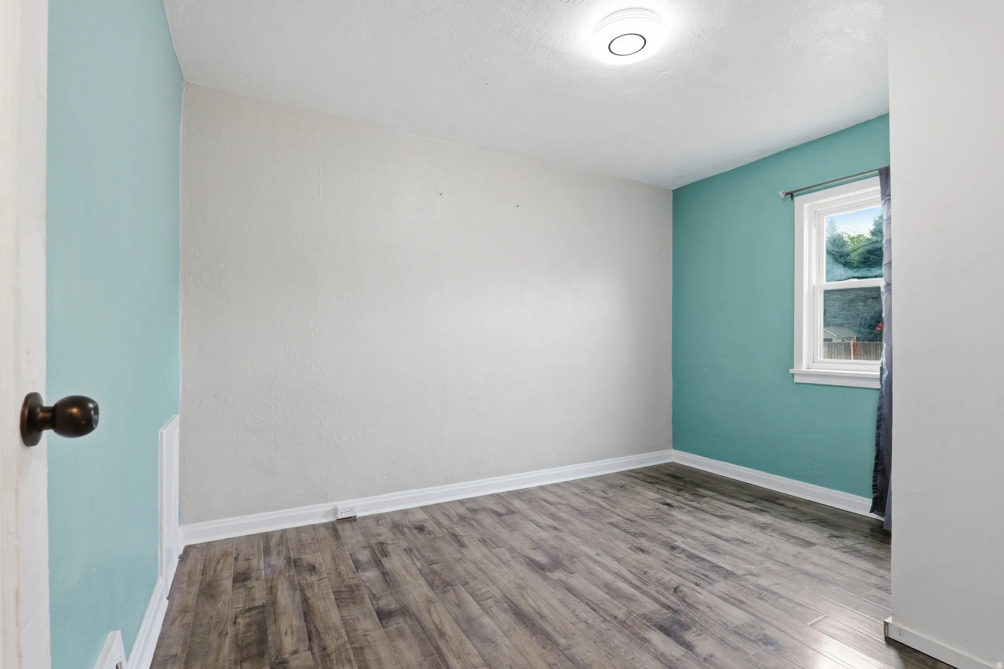 Room featuring wood-finish flooring, white baseboards, and a window with white trim