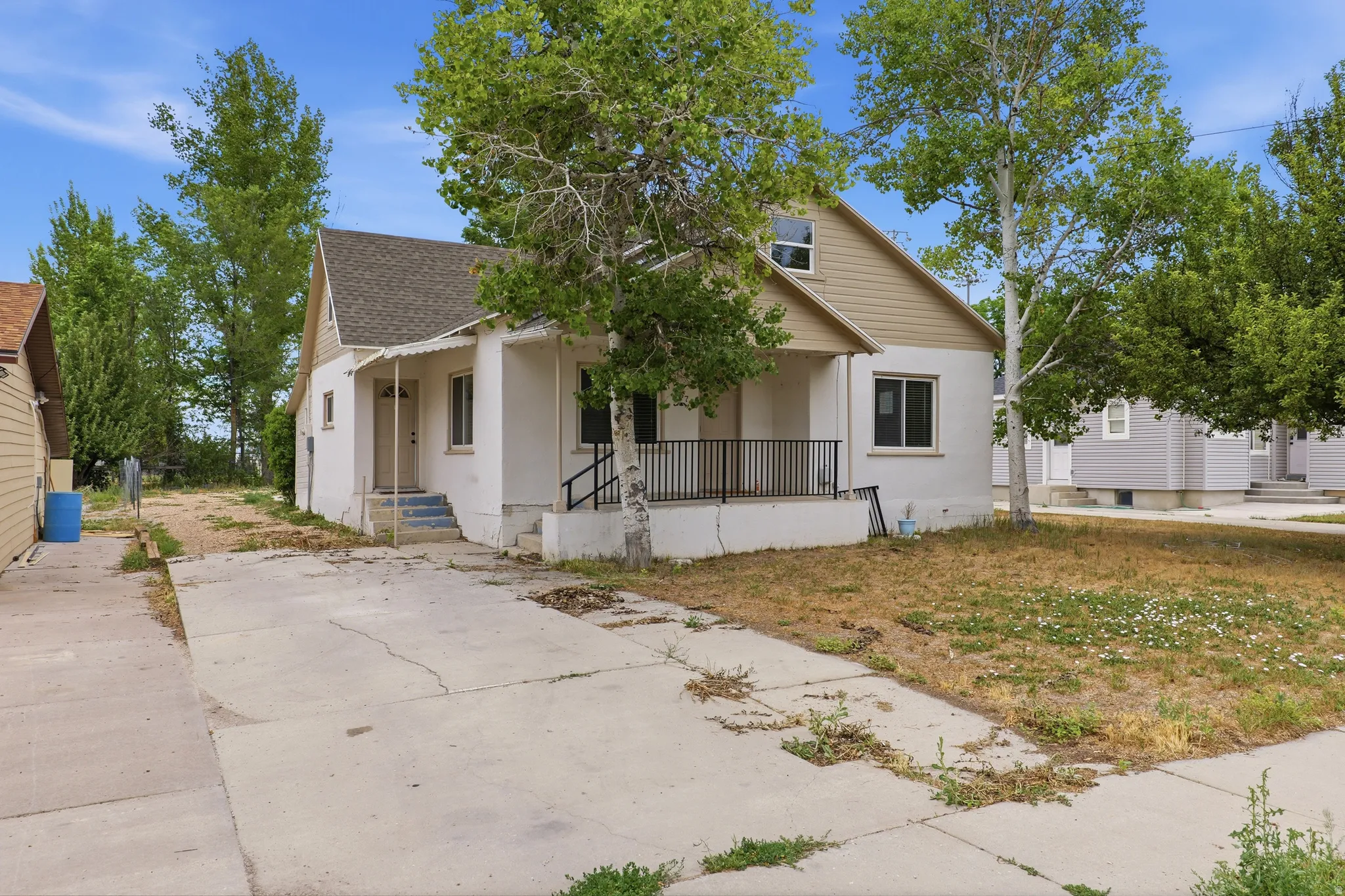 Two-story residence featuring a covered front porch with black metal railing, concrete driveway, and a partially covered entry