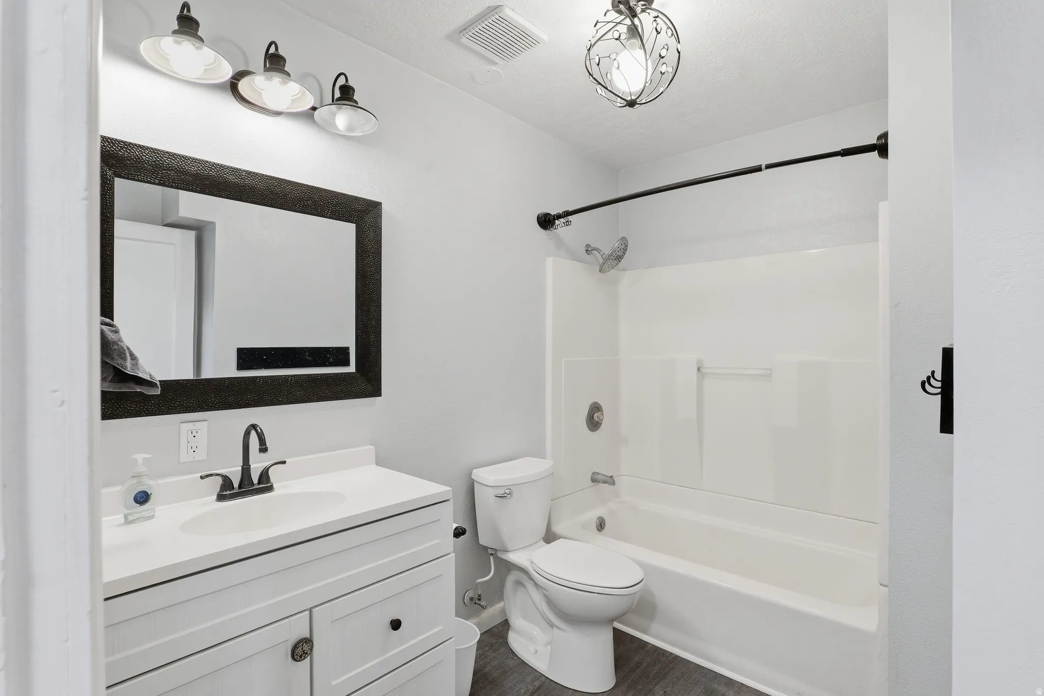 Bathroom featuring a white vanity with integrated sink, dark wood-finish flooring, a combination bathtub and shower with a curved shower rod, and an ornamental ceiling light fixture