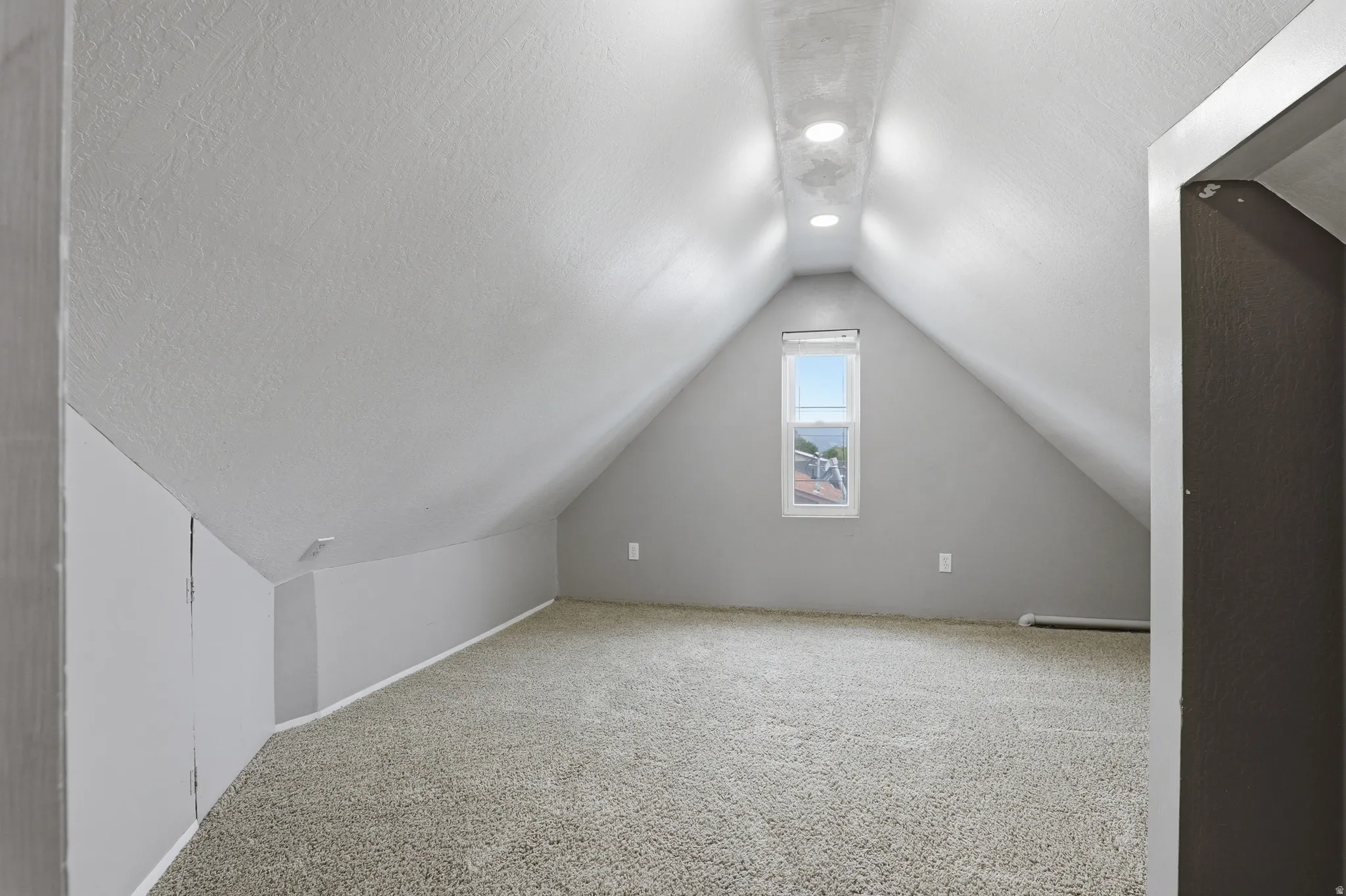 Attic space featuring sloped ceilings, recessed lighting, and a window