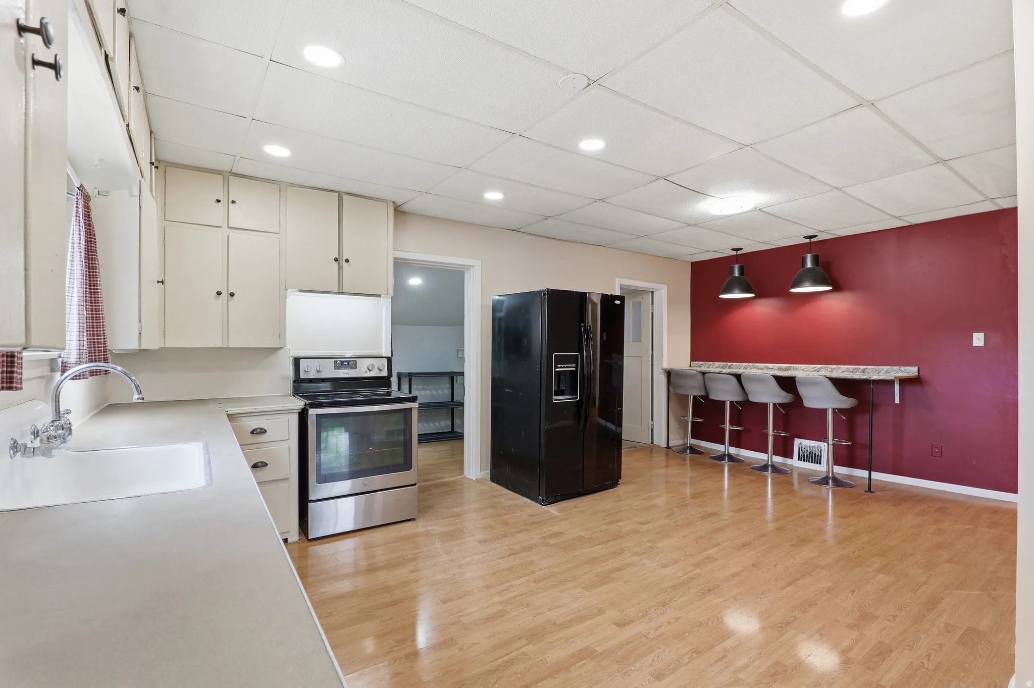 Kitchen featuring light-finish cabinetry, stainless steel range, light countertops, wood-finish flooring, and a breakfast bar with pendant lighting