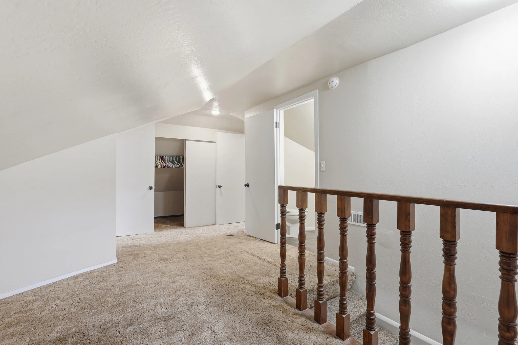 Carpeted loft area featuring a sloped ceiling, multiple closet spaces with sliding doors, and a wood balustrade