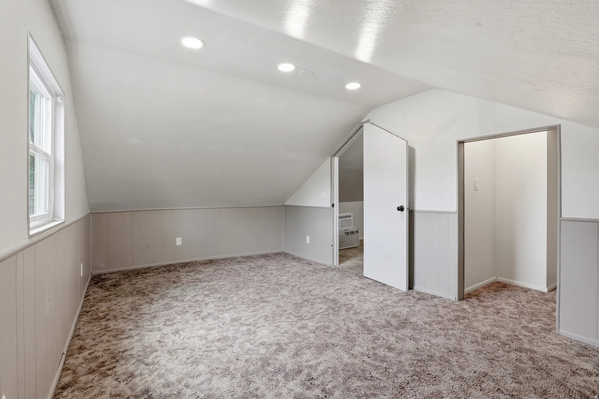 Carpeted room featuring sloped ceilings, recessed lighting, a white framed window, and wainscoting