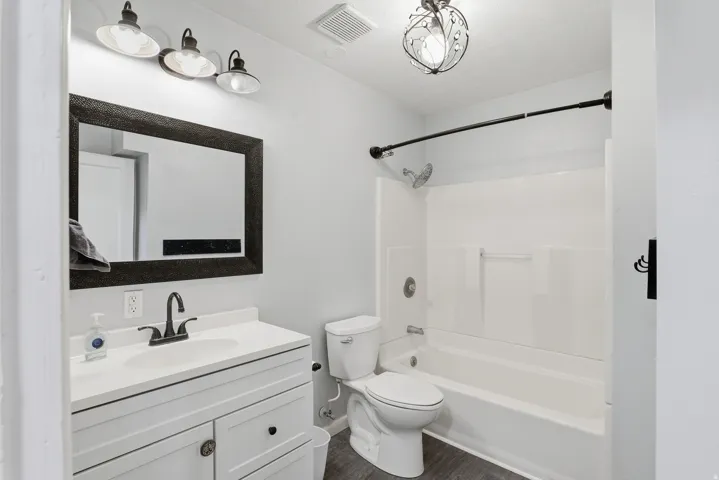 Bathroom featuring a white vanity with integrated sink, dark wood-finish flooring, a combination bathtub and shower with a curved shower rod, and an ornamental ceiling light fixture