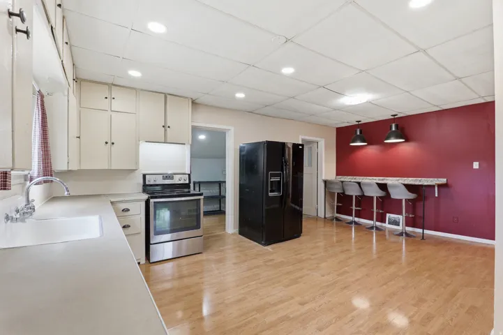 Kitchen featuring light-finish cabinetry, stainless steel range, light countertops, wood-finish flooring, and a breakfast bar with pendant lighting