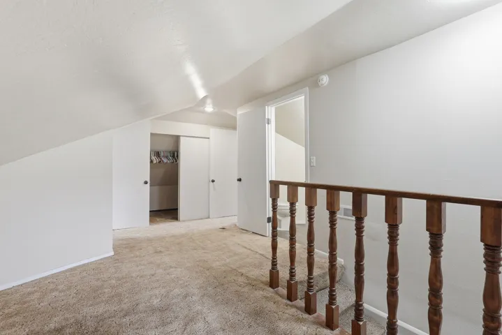 Carpeted loft area featuring a sloped ceiling, multiple closet spaces with sliding doors, and a wood balustrade