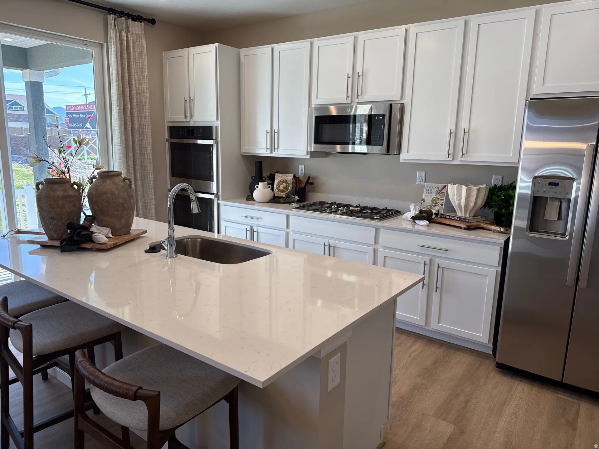 Kitchen featuring white cabinetry, stainless steel appliances, a gas range, double wall ovens, and a center island with a sink and ample counter space