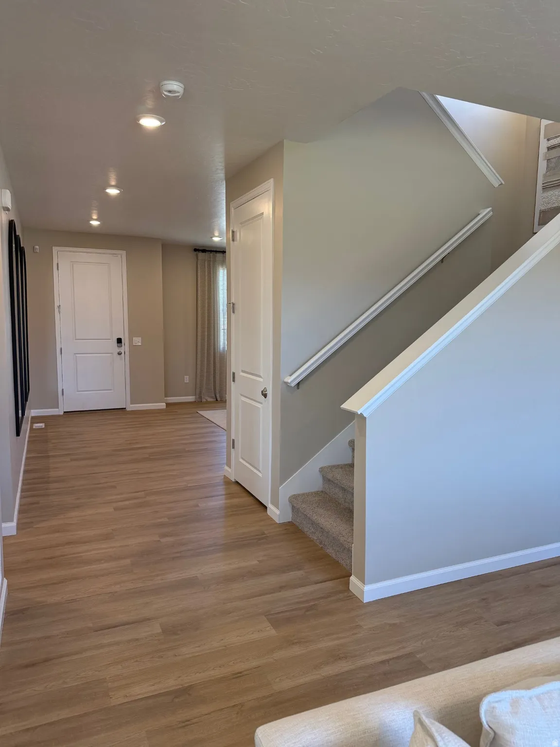 Inviting entryway featuring wood-finish flooring extending through the hall, recessed lighting, and a staircase with carpeted treads and a white railing