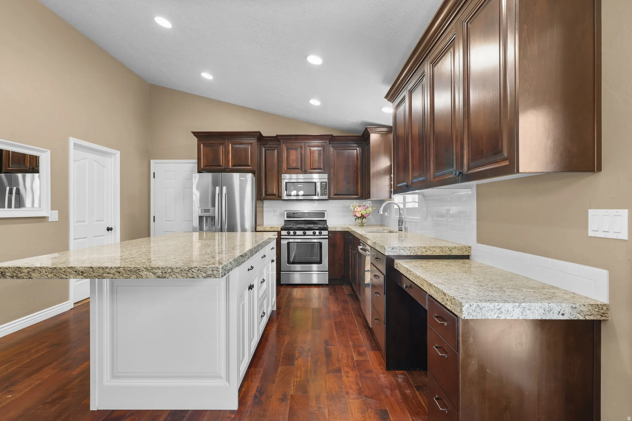 Kitchen featuring a large central island with light granite countertops, dark wood cabinetry, stainless steel appliances, and wood-finish flooring