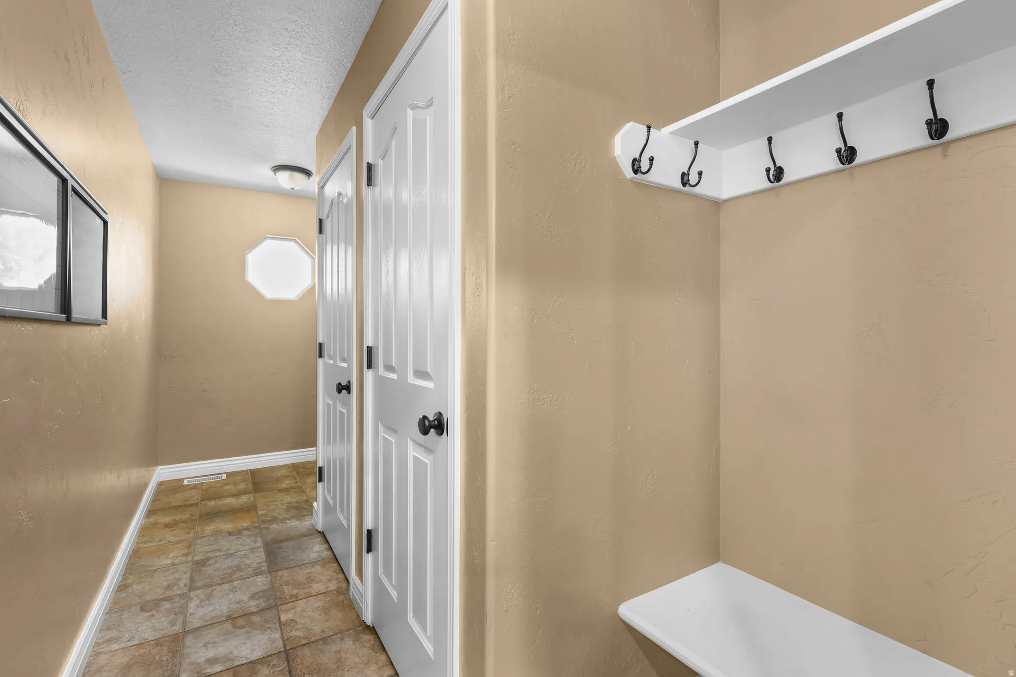 Entryway featuring a built-in white shelving unit with black hooks and a matching bench