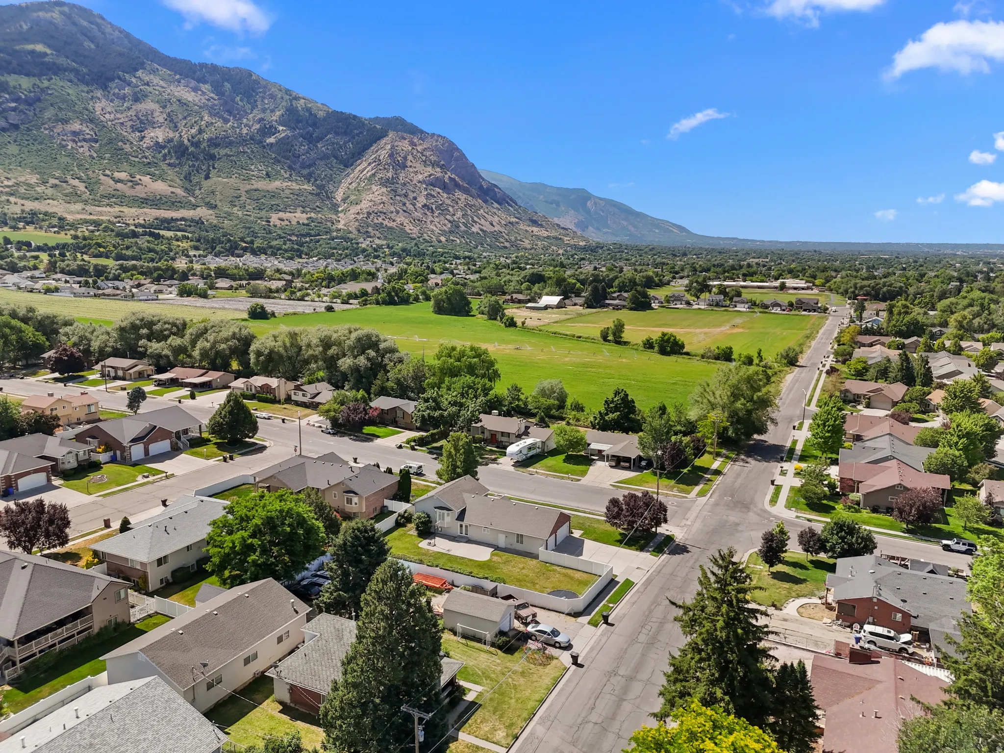 Mountainous landscape with expansive green fields and a residential neighborhood featuring paved roads and mature trees
