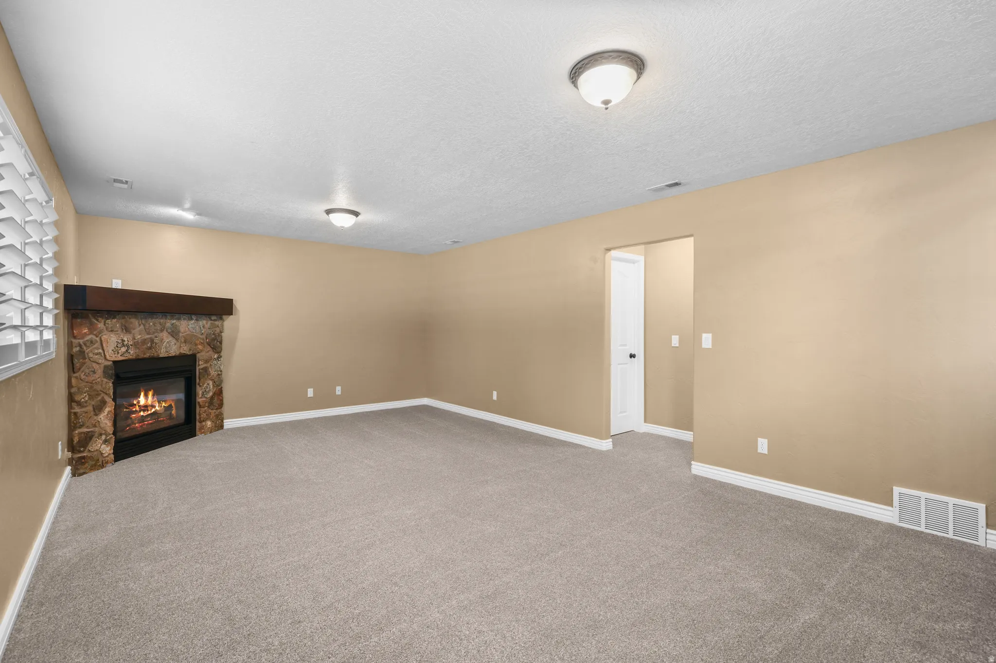 Spacious living area featuring a stone-clad fireplace with a wood mantel, light gray carpeting, and neutral wall tones