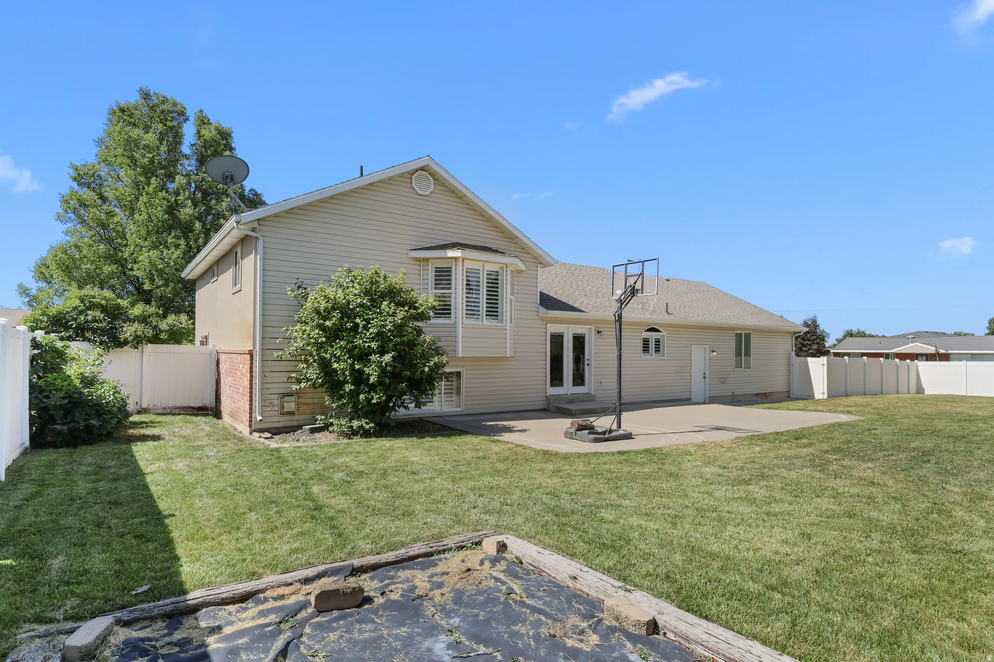 Expansive backyard with a large concrete patio, mature landscaping, and white privacy fencing