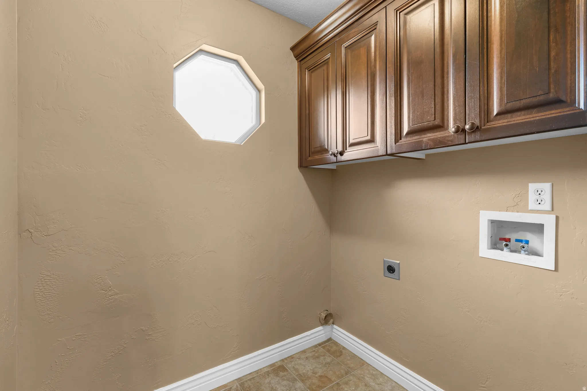 Laundry room featuring a hexagonal window, wood cabinetry, tile flooring, and a washer/dryer hookup with electrical outlet