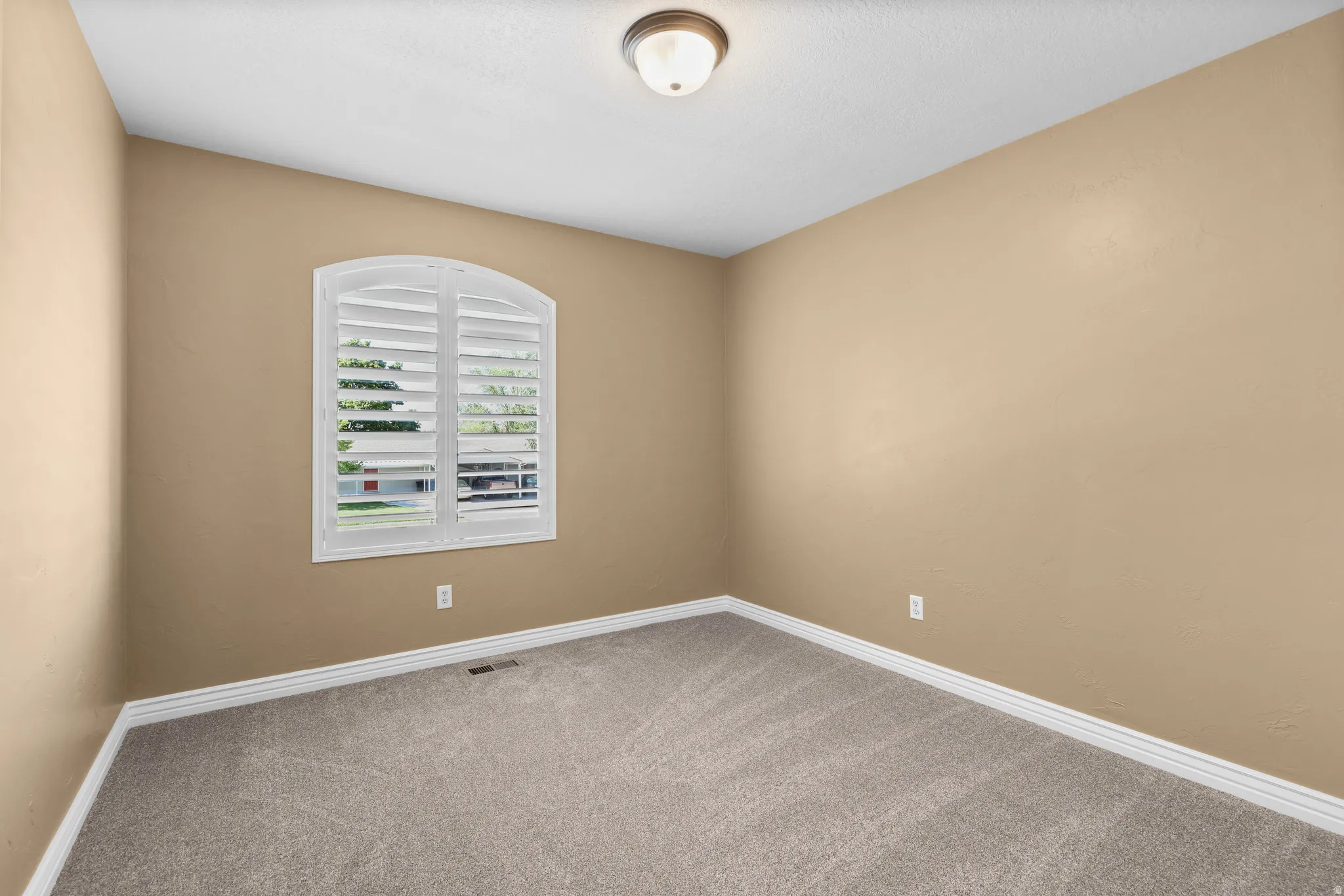 Arched window featuring white plantation shutters, neutral tone walls, white trim, and textured carpeting