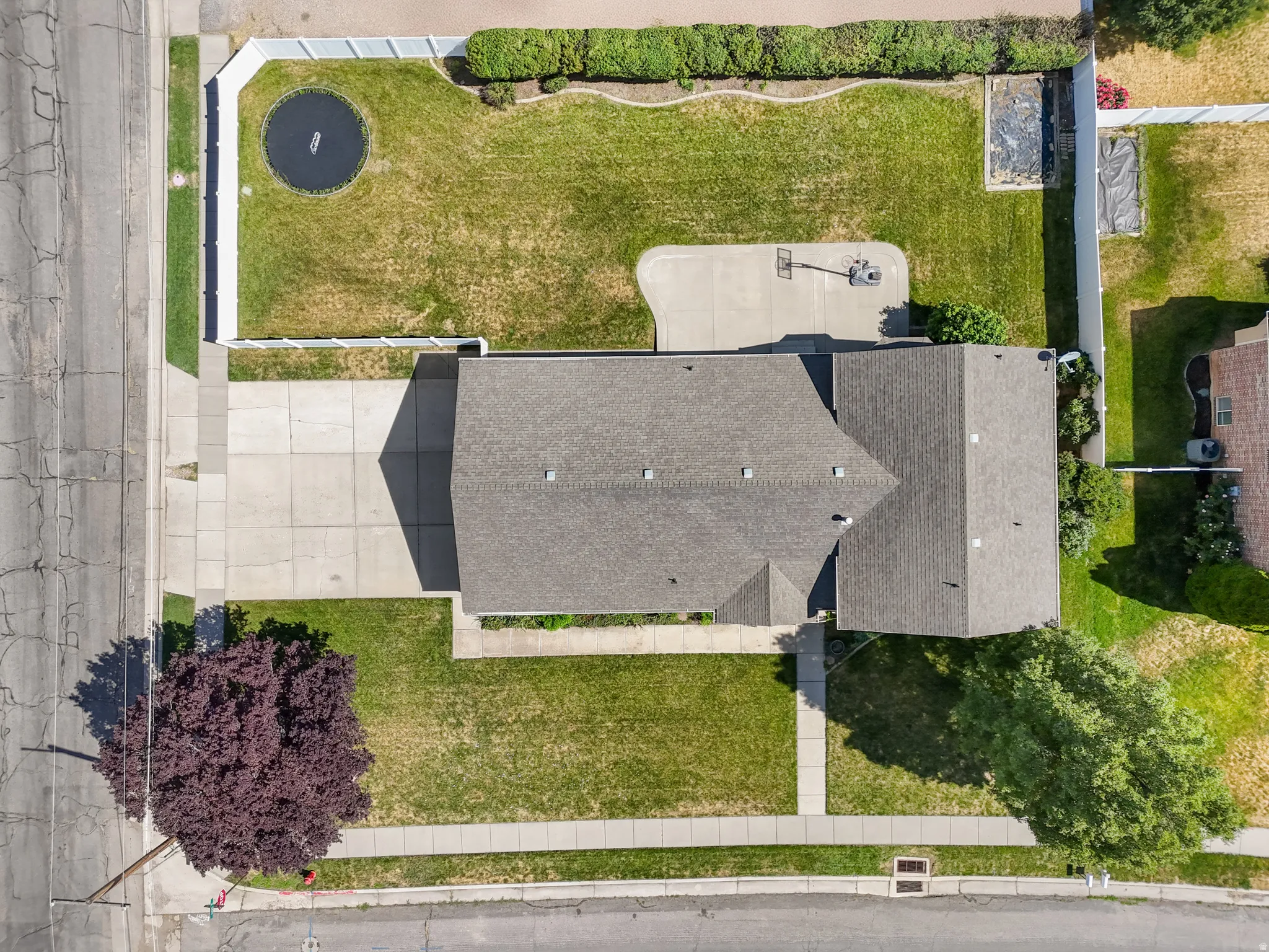 Expansive property featuring a multi-gabled roofline, concrete driveway, and a spacious backyard with a hardscaped basketball area