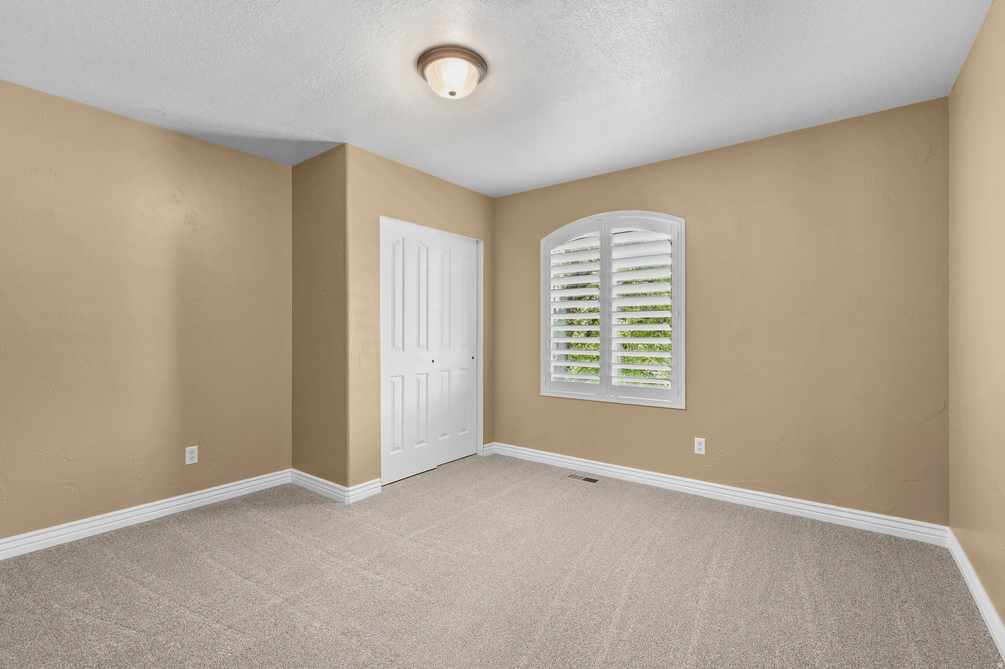 Carpeted interior space featuring neutral tone walls, white baseboards, and a white bi-fold closet door