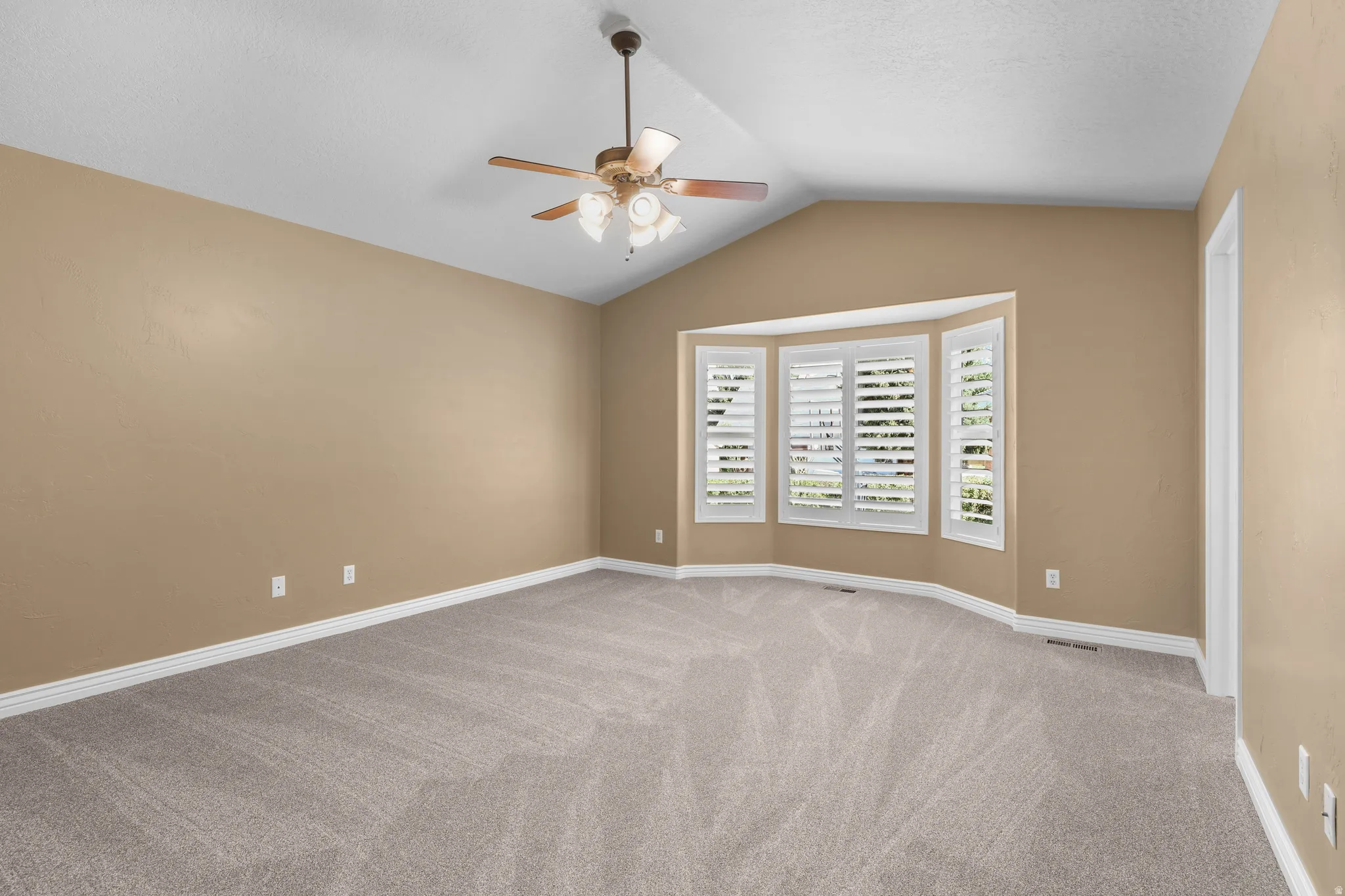 Primary Bedroom with vaulted ceilings, ceiling fan, and neutral-toned carpeting