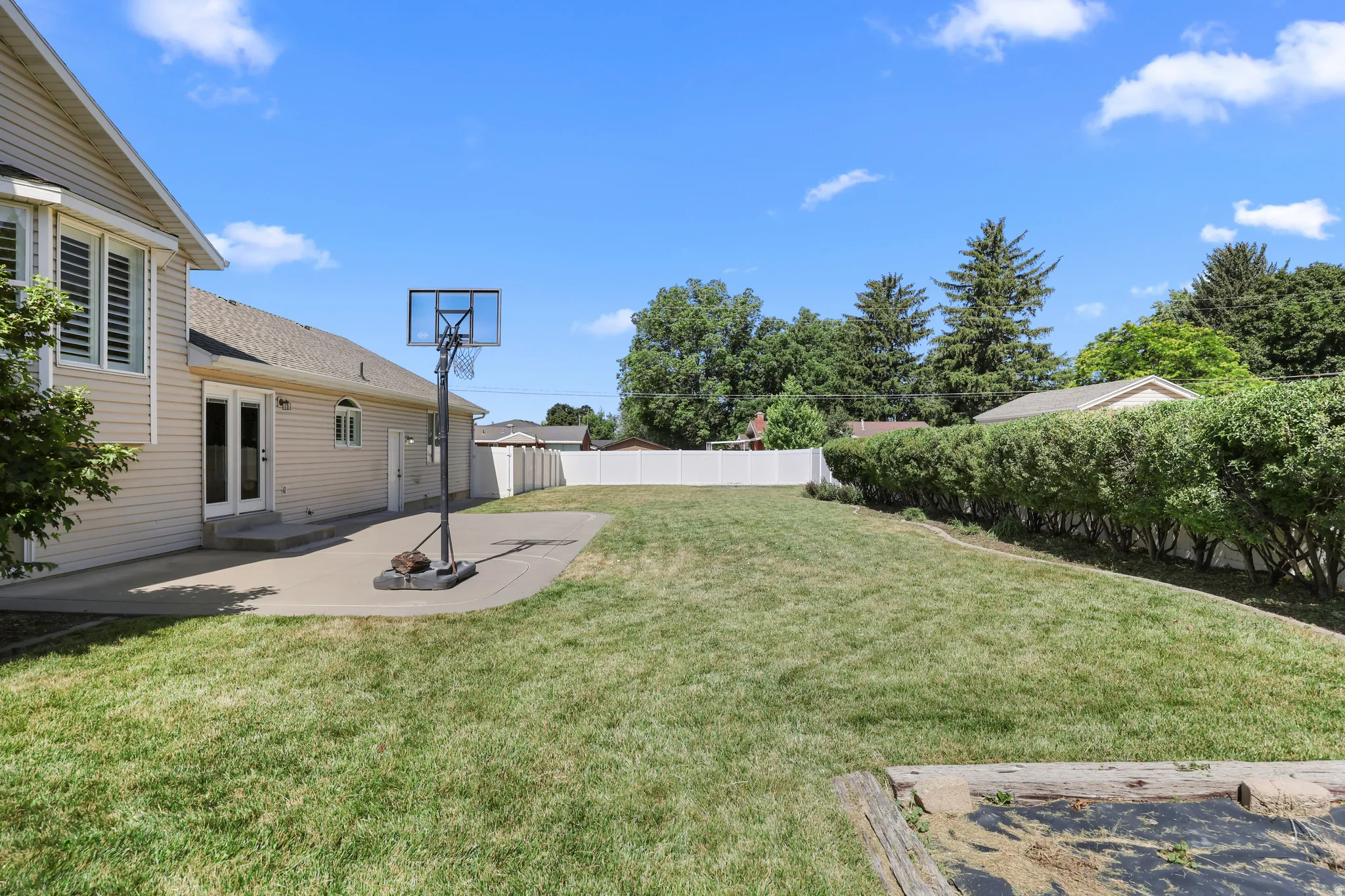 Expansive backyard featuring a large concrete patio, mature green landscaping, and a privacy fence