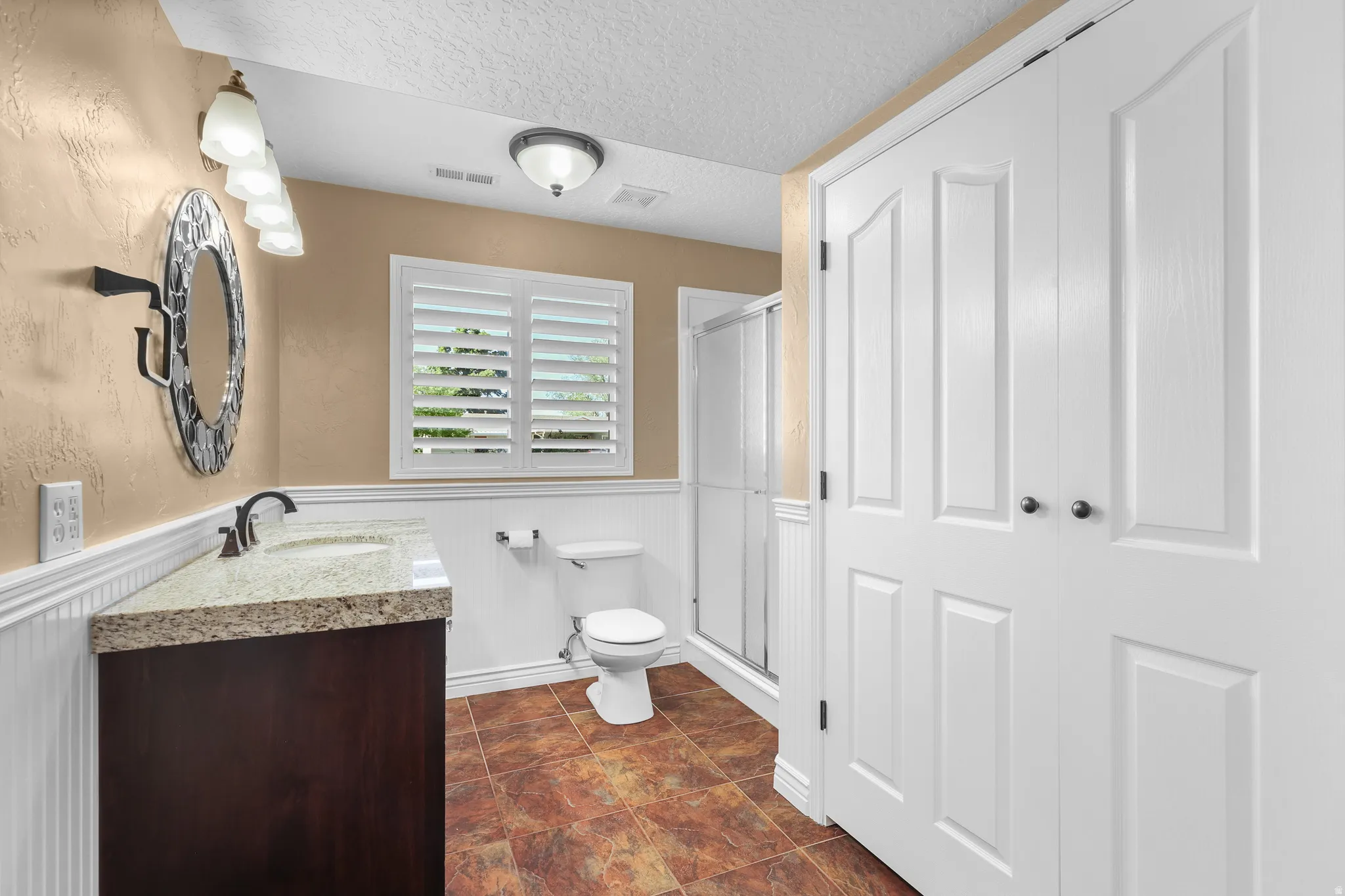 Bathroom featuring a dark wood-finish vanity with a light granite countertop, a white toilet, and a glass-enclosed shower
