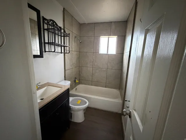 Bathroom featuring a dark wood vanity with a light-colored countertop and integrated sink, a built-in bathtub with a shower head, and light-toned wall tiling extending to the ceiling