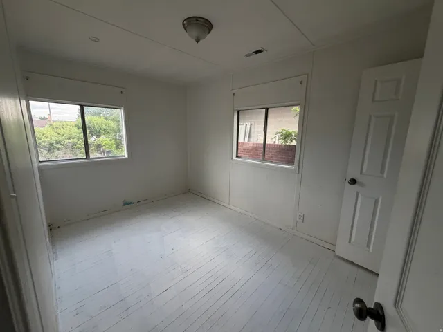 Room with painted wood-plank flooring, two windows, and a panel door