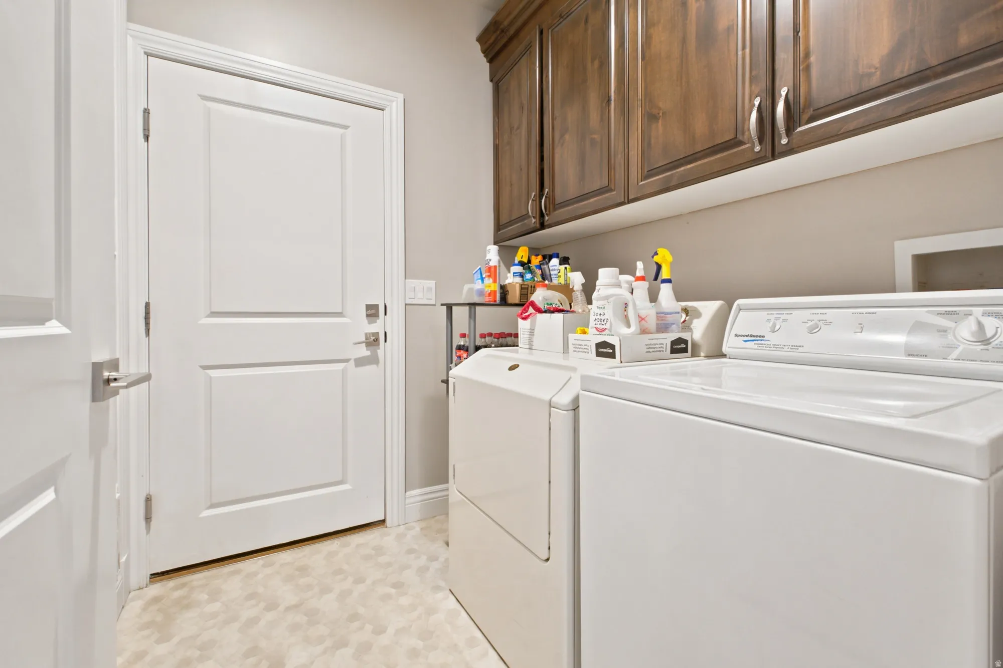 Laundry area with wood-finish cabinetry, white paneled door, and light-toned flooring