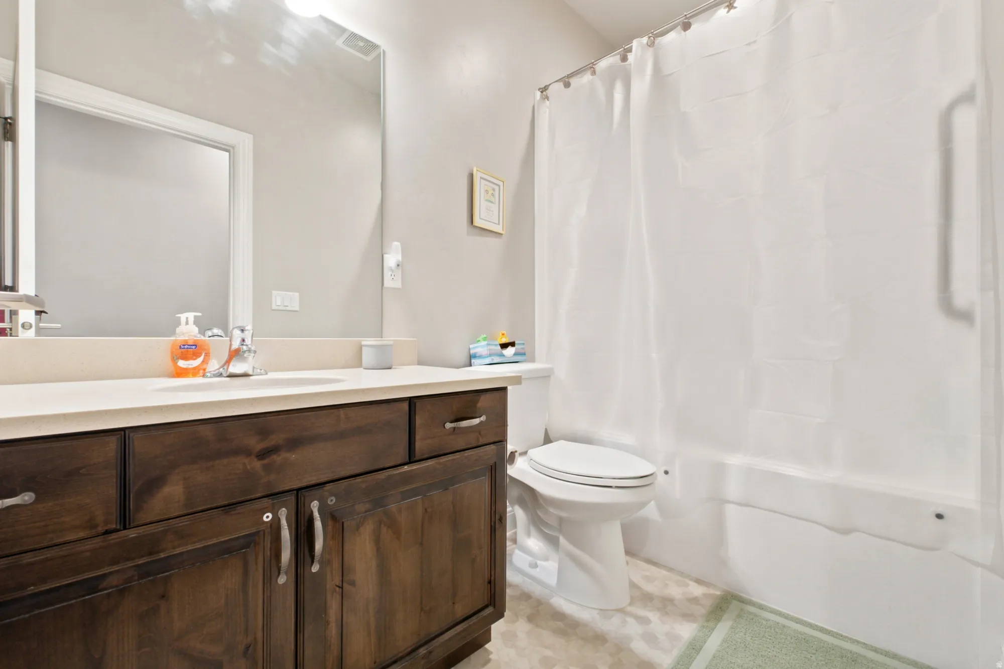 Bathroom featuring a dark wood-finish vanity with a light countertop, a single basin sink, a large wall mirror, and a full-size bathtub with shower