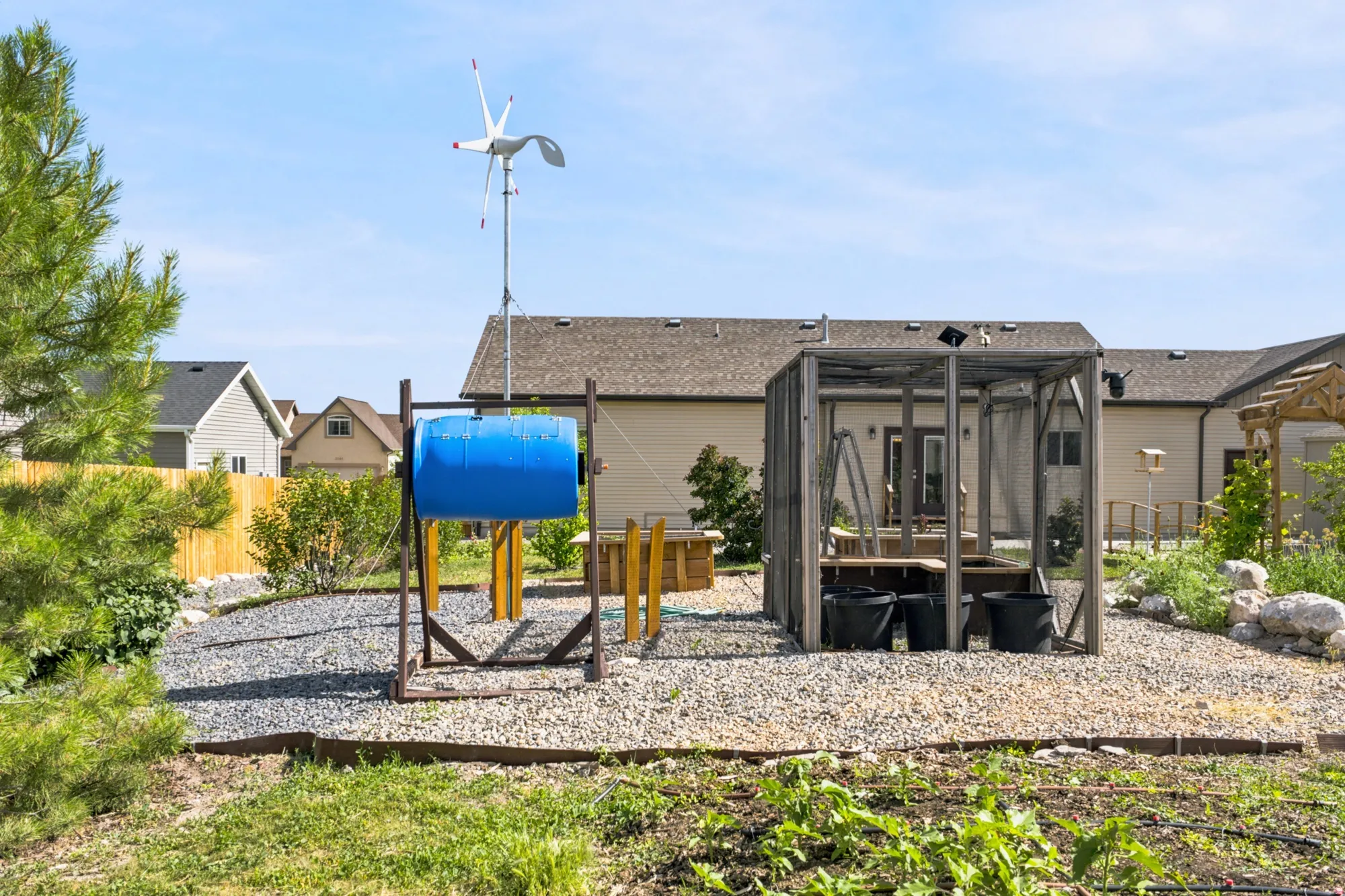 Gravel backyard area featuring a compost tumbler, a small wind turbine, and a screened enclosure