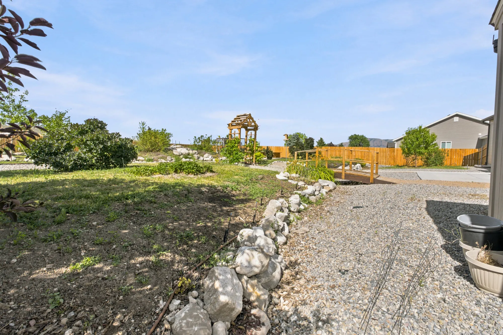 Expansive outdoor space featuring a gravel path, a decorative wooden bridge, and a rock border
