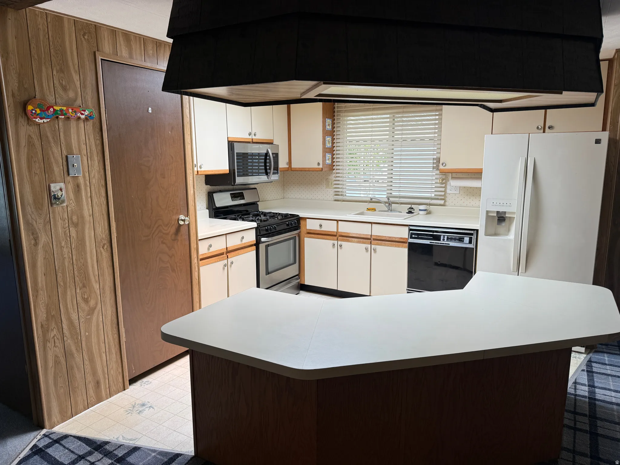 Kitchen featuring an L-shaped peninsula with white countertops, light wood-finish cabinetry, white appliances, and a stainless steel gas range with a matching microwave