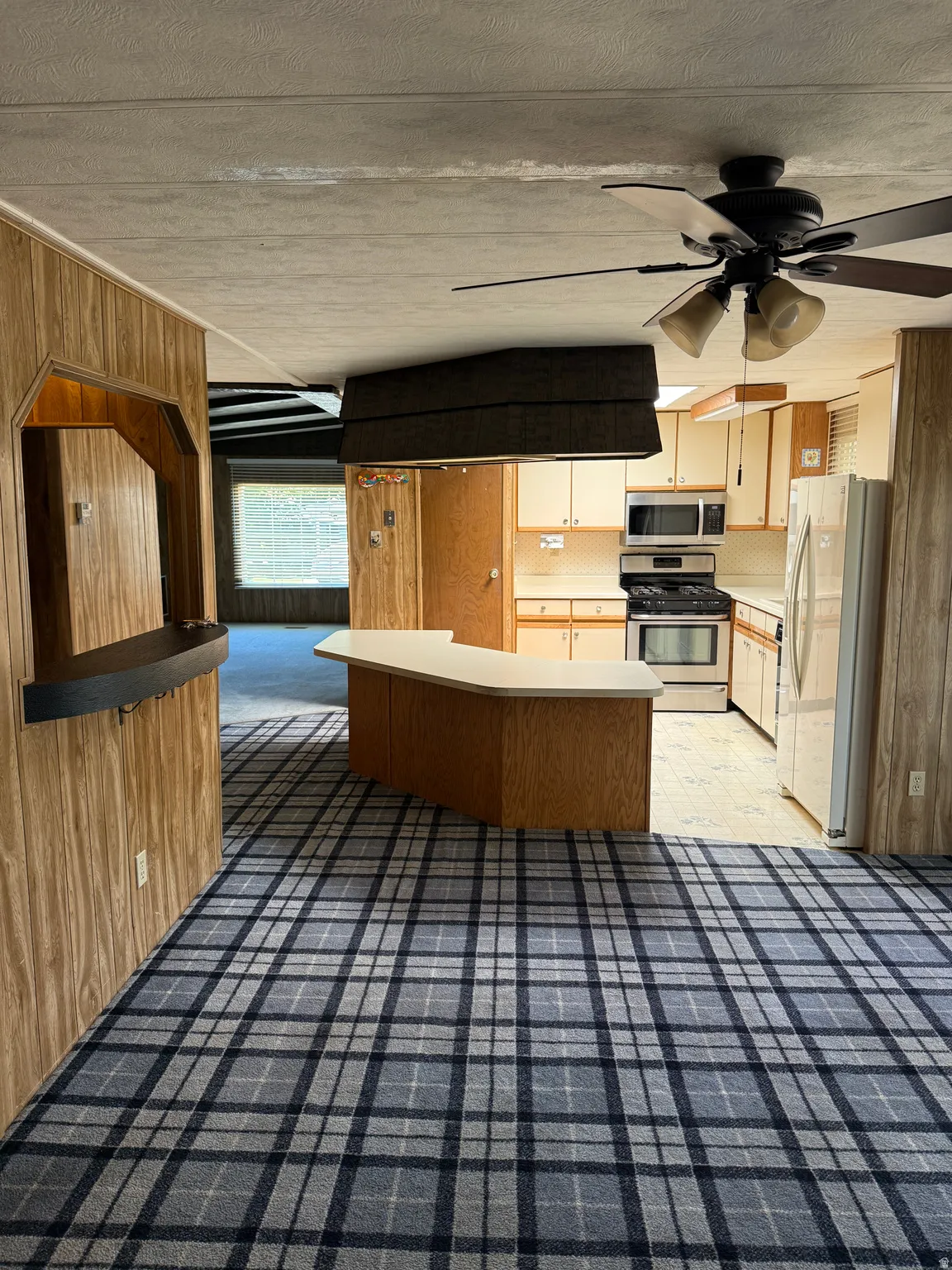 Open-concept living area featuring a kitchen with light wood-finish cabinetry, a built-in microwave, and a gas range