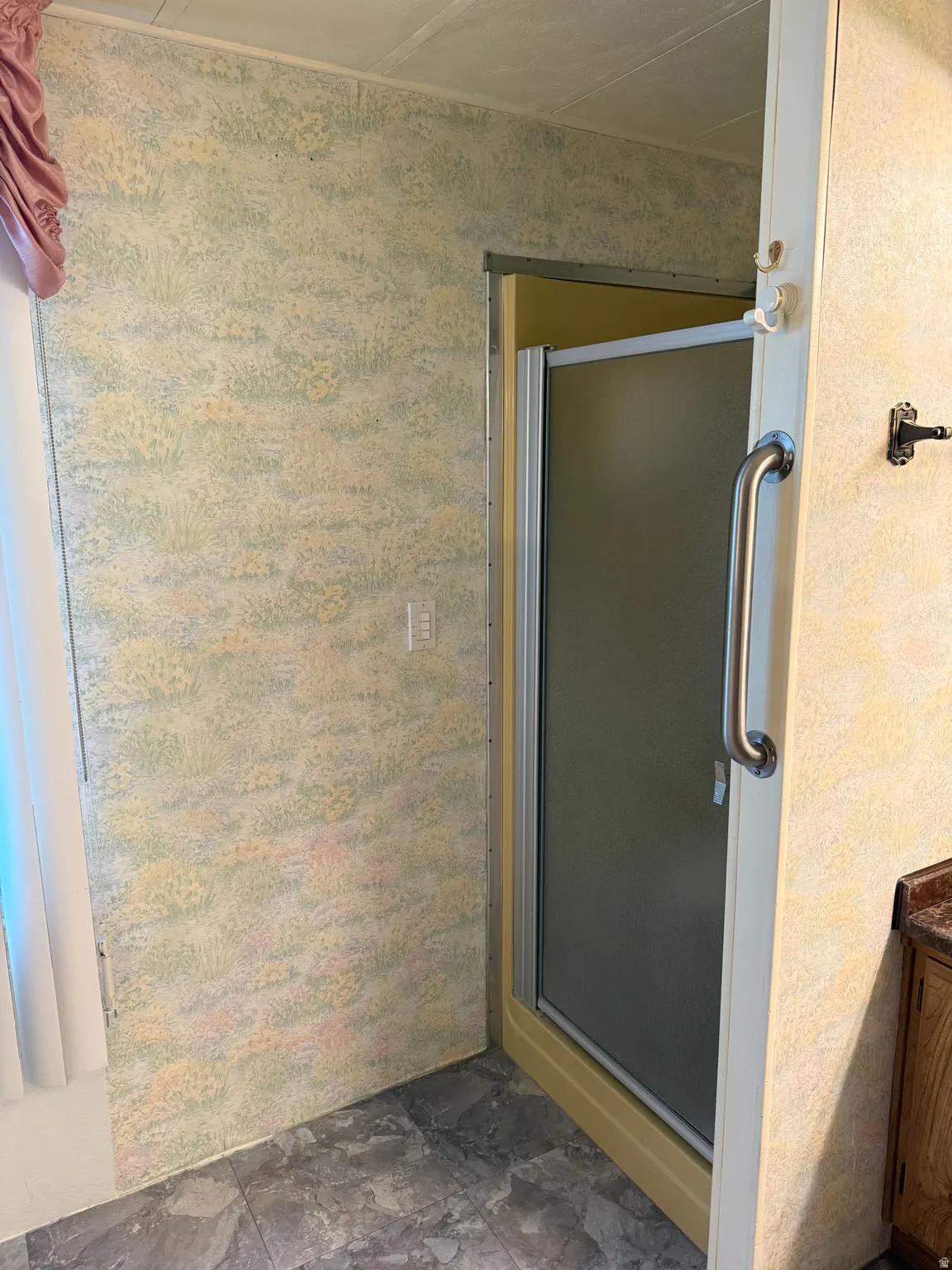 Frosted glass shower enclosure with a stainless steel grab bar, set against patterned wallpaper and grey tile flooring