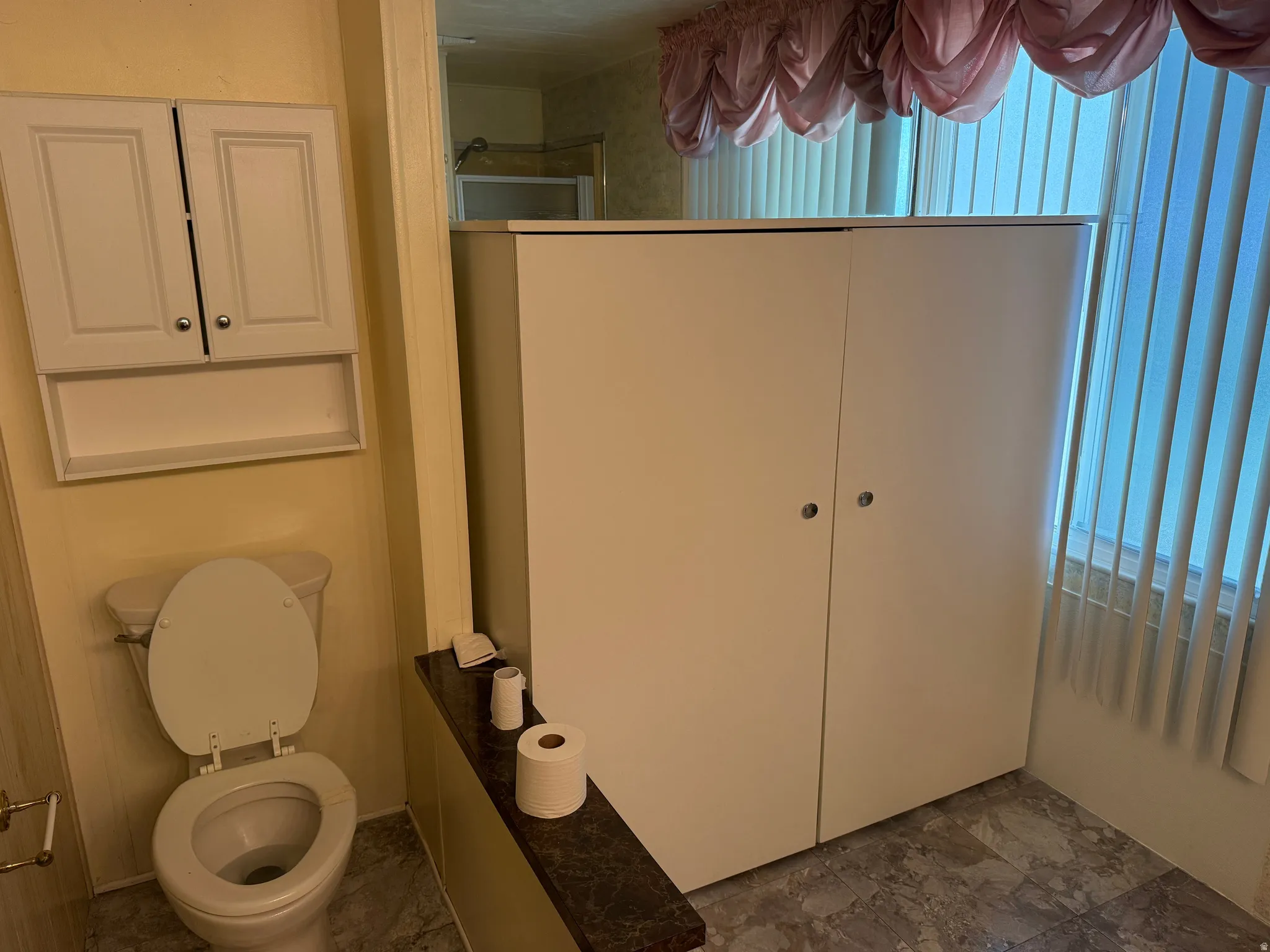 Bathroom featuring a white wall-mounted cabinet, a built-in white storage unit, and a window with vertical blinds