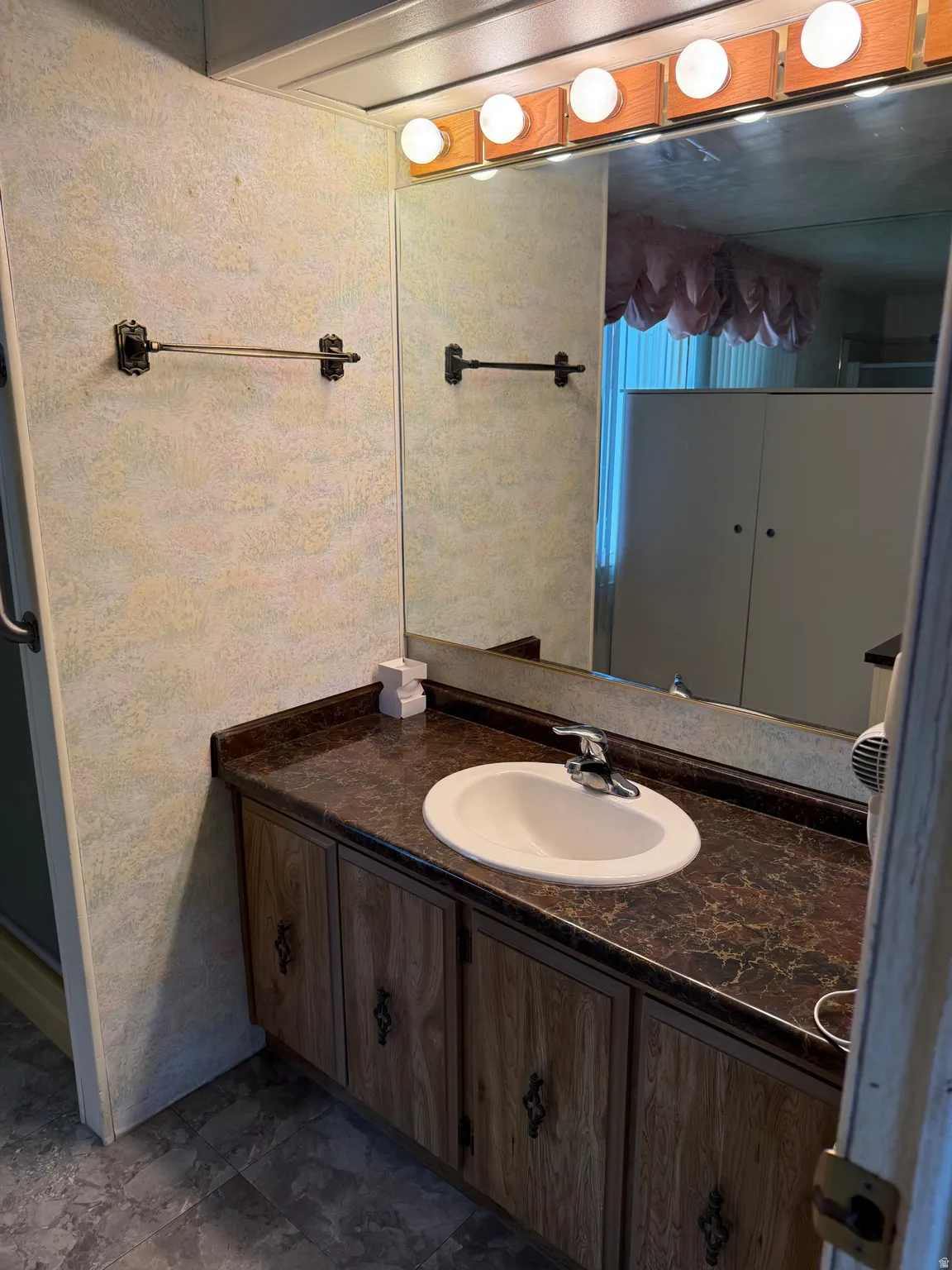 Bathroom vanity featuring an integrated sink, laminate countertop, and wood-finish cabinetry with decorative hardware