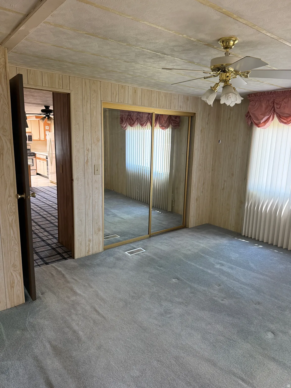 Carpeted room featuring a ceiling fan with integrated lighting, mirrored closet doors, and wood paneling