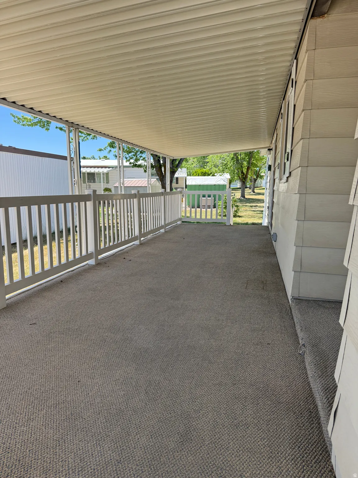 Covered porch featuring durable outdoor carpeting, white railing, and a slatted overhead canopy