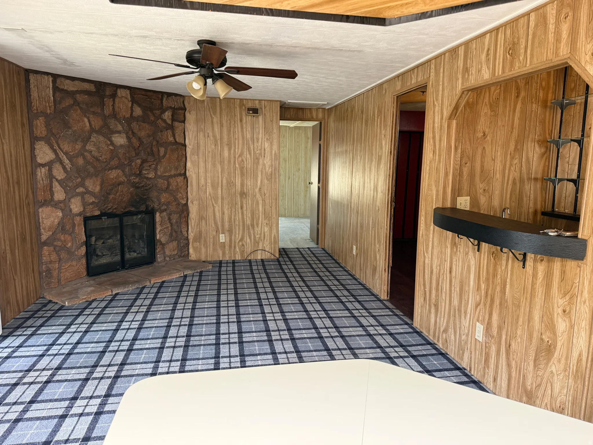 Interior space featuring wood-finish wall paneling, a stone-clad fireplace, and a plaid-patterned carpet
