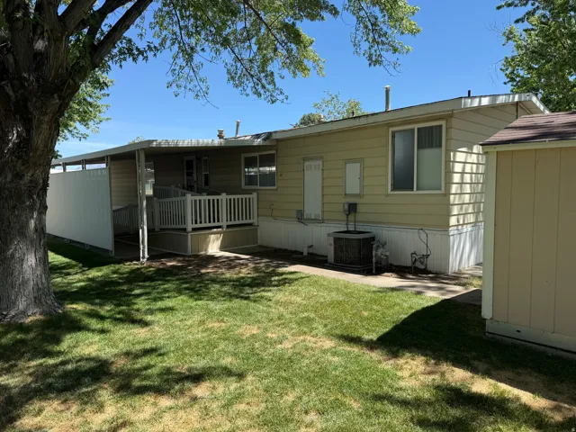 Rear exterior featuring a covered porch with white railing, ramp access, and a manicured lawn