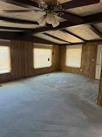Spacious room featuring vaulted ceilings with exposed beams, paneled wood-finish walls, and plush carpeting
