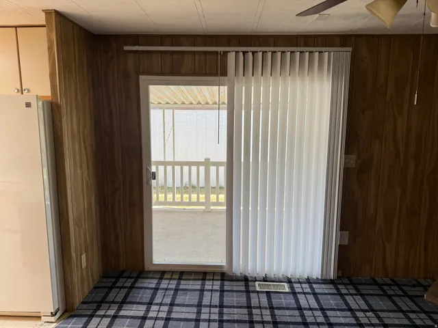 Sliding glass door with vertical blinds offering access to an outdoor patio with white railing