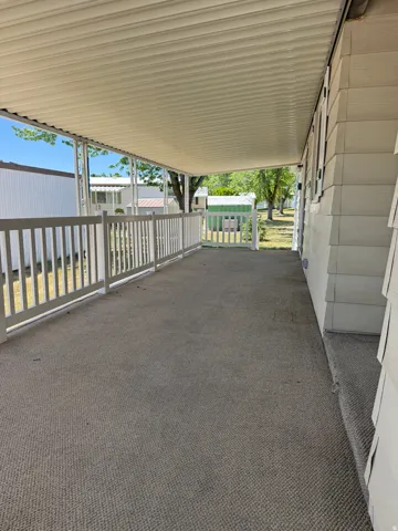 Covered porch featuring durable outdoor carpeting, white railing, and a slatted overhead canopy