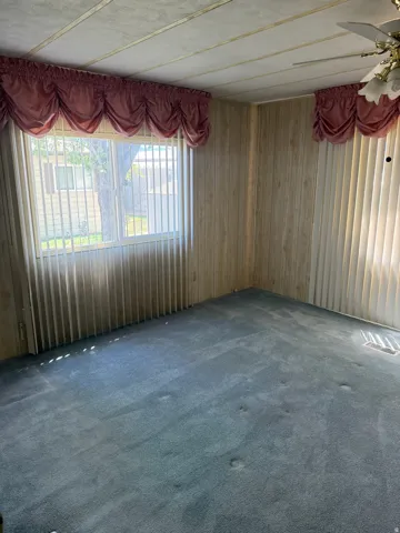 Room featuring paneling walls, a light blue carpeted floor, and a window with vertical blinds