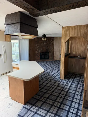 Open-concept living area featuring a central island with a light-toned countertop, a stone fireplace, and wood-finish paneling