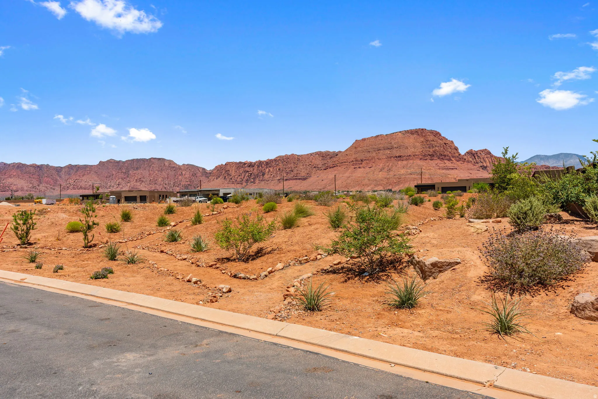 Desert landscape on view protection lot featuring sparse, drought-tolerant plantings, exposed red earth, and distant red rock mountains